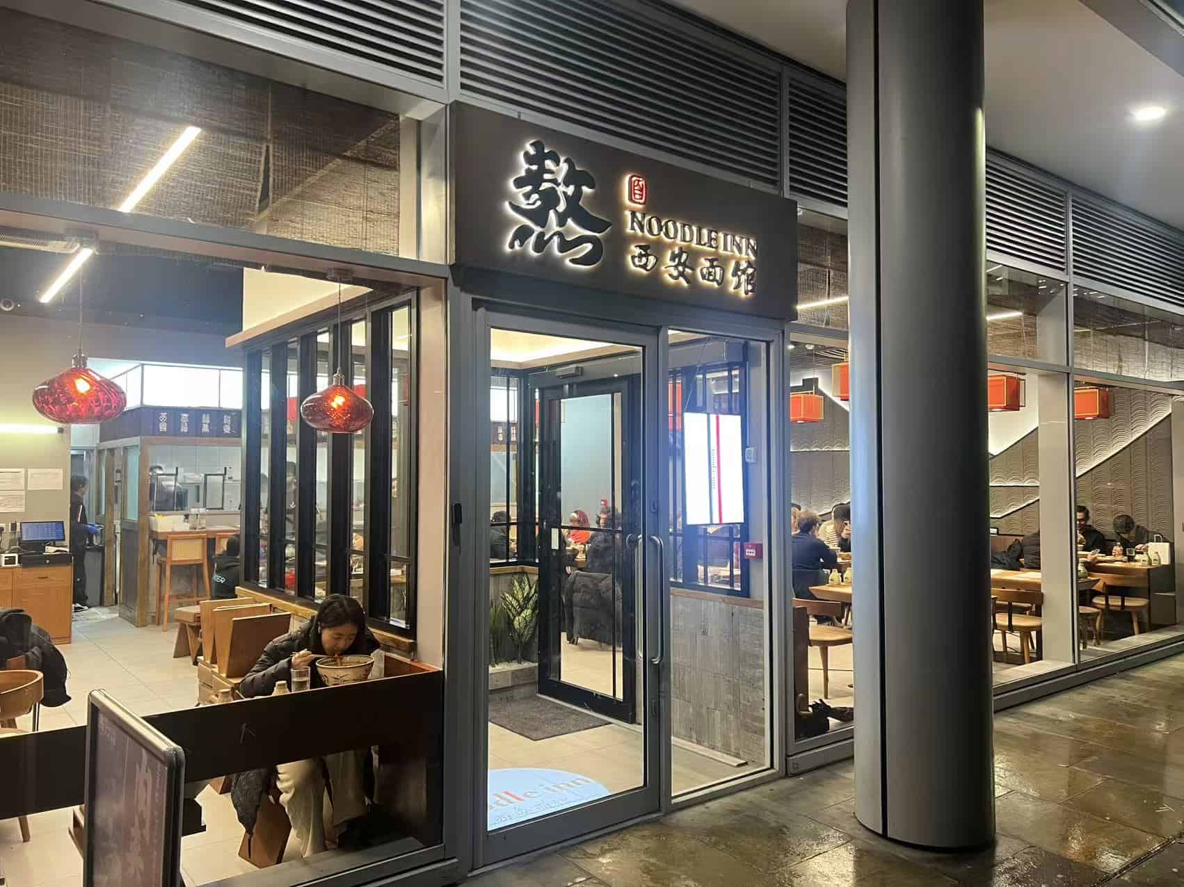 Modern Noodle Inn restaurant entrance with glass doors and interior seating area.