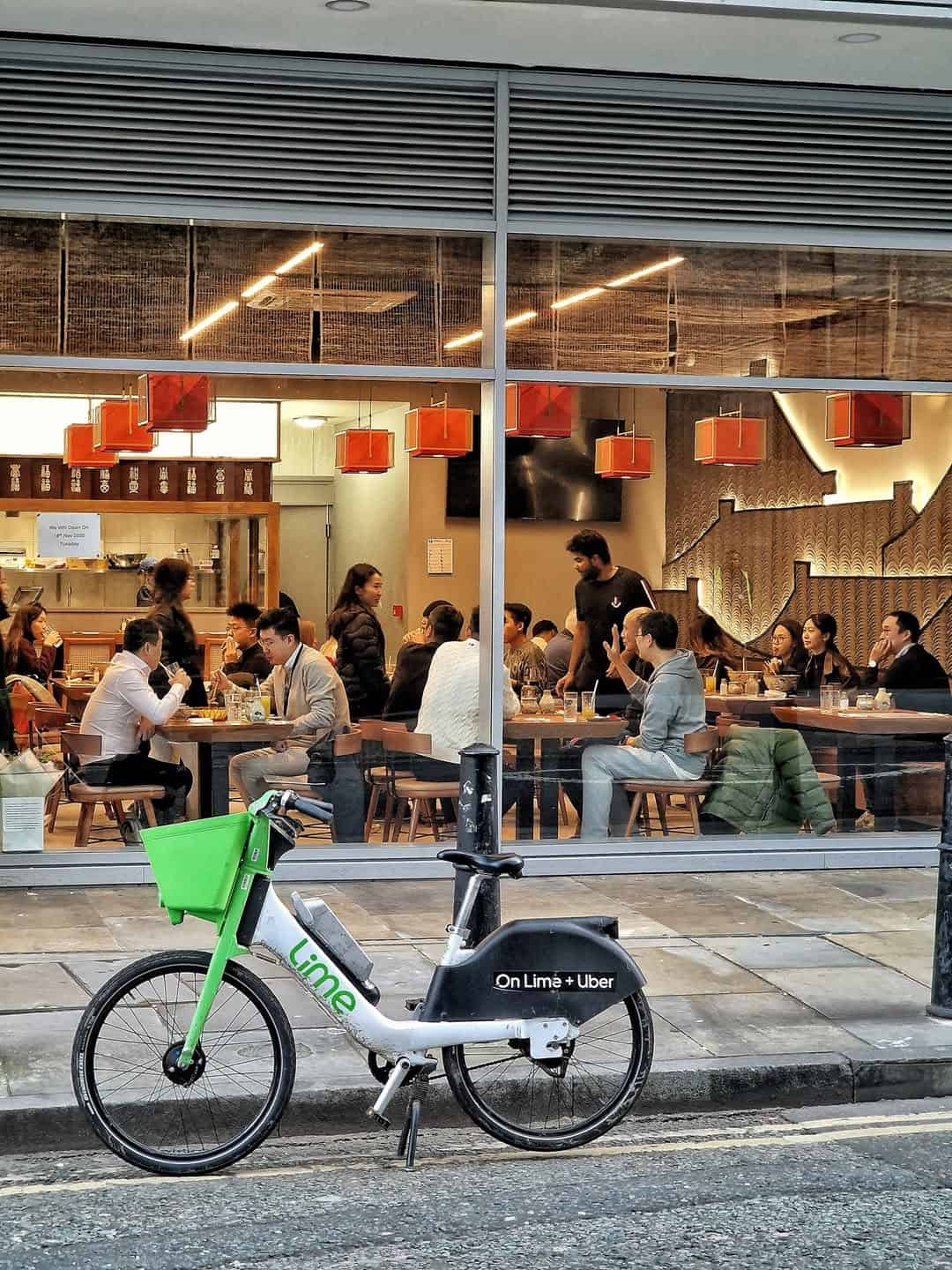 Modern Noodle Inn restaurant with customers dining inside, seen through large glass window.
